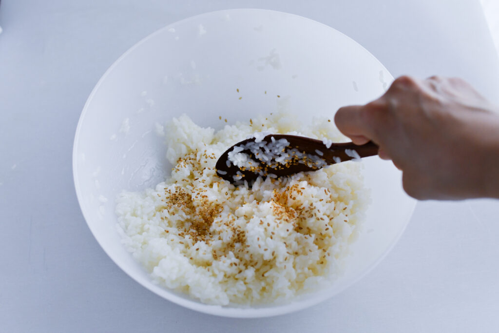 温かいご飯に合わせ酢、白ごまを入れながら、しゃもじで切り混ぜてカンタン酢めしを作る。俵型にまとめておく。